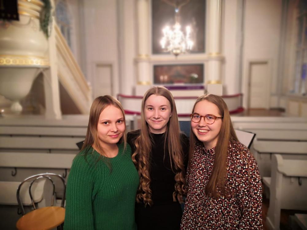 Kolme nuorta naista hymysuin ja kaulakkain Kannuksen kirkossa.