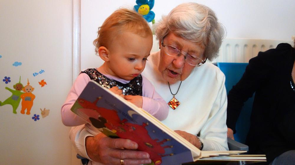 Iäkäs nainen lukee satukirjaa pienelle lapselle.