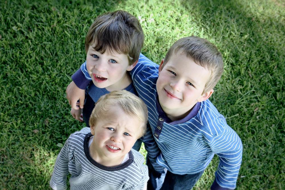Kolme pikkupoikaa katsoo kameraan ja hymyilee.