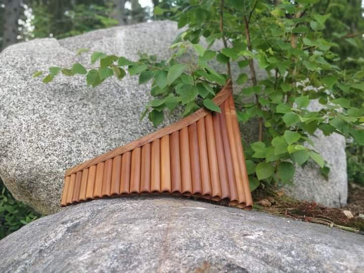 ILTAMUSIIKKI Kesällä otettu kuva ulkona, panhuilu nojaa isoa kiveä vasten